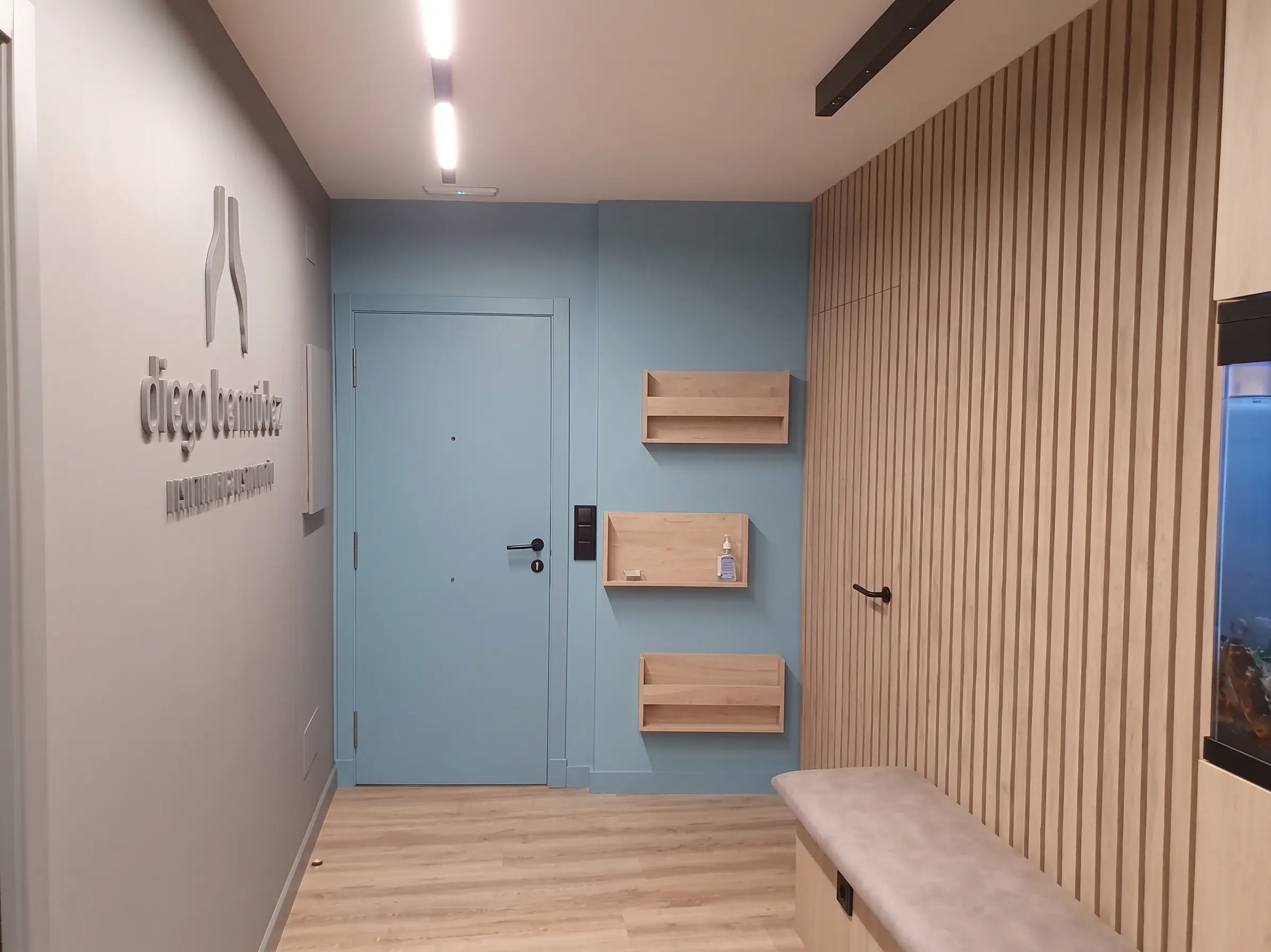 Recepción de la clínica, con el logotipo de Diego Bermúdez en la pared, una puerta azul y un banco de espera